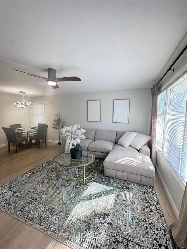 living room with ceiling fan, baseboards, and wood finished floors