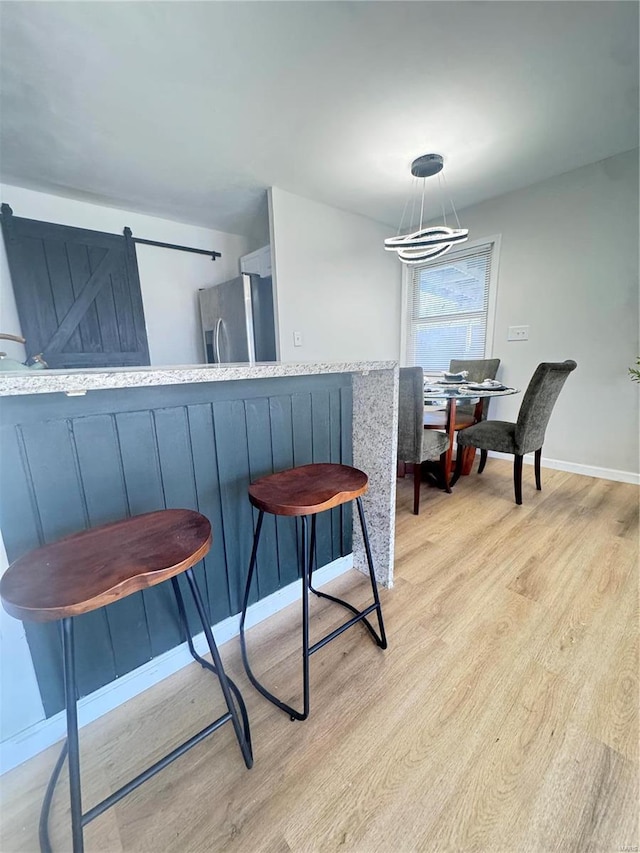 dining room featuring a barn door, light wood-style flooring, and baseboards