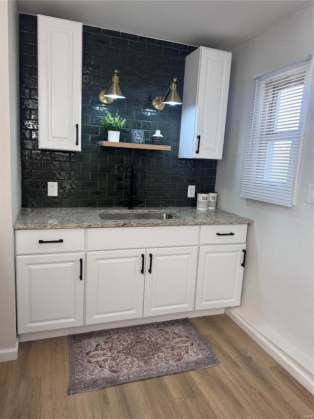 bar with tasteful backsplash, light wood-type flooring, a sink, and baseboards