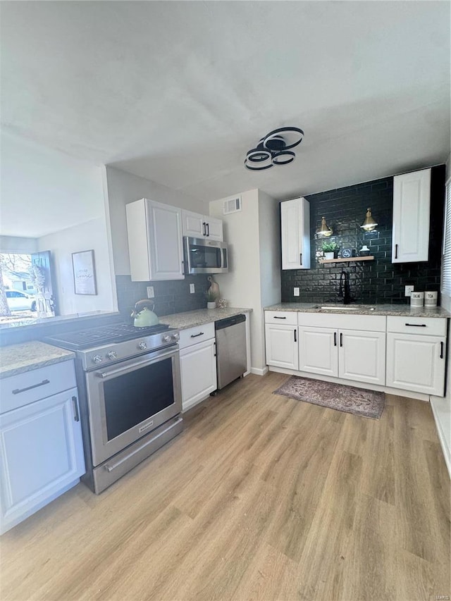 kitchen with visible vents, appliances with stainless steel finishes, light wood-style floors, white cabinetry, and a sink