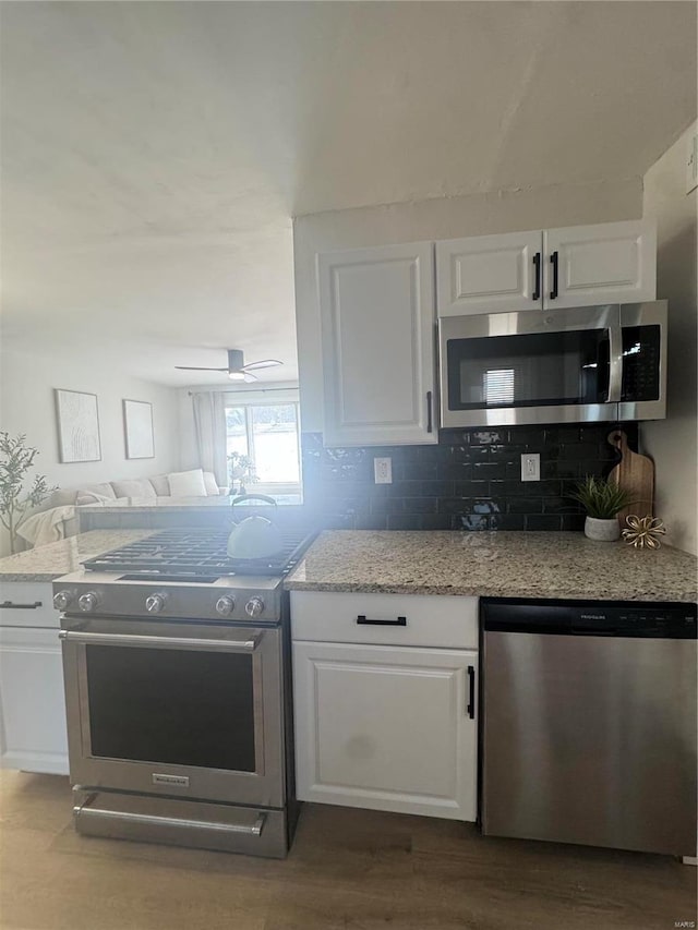 kitchen with dark wood finished floors, stainless steel appliances, decorative backsplash, white cabinets, and light stone countertops