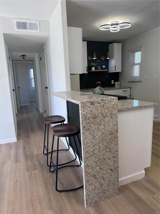 kitchen with a peninsula, white cabinetry, light wood-style flooring, and visible vents