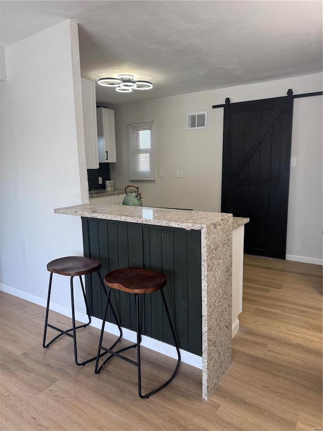 kitchen with light wood finished floors, a breakfast bar area, visible vents, a barn door, and a peninsula