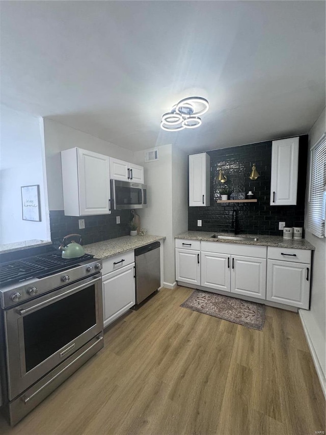 kitchen featuring light wood-style flooring, stainless steel appliances, a sink, visible vents, and white cabinets