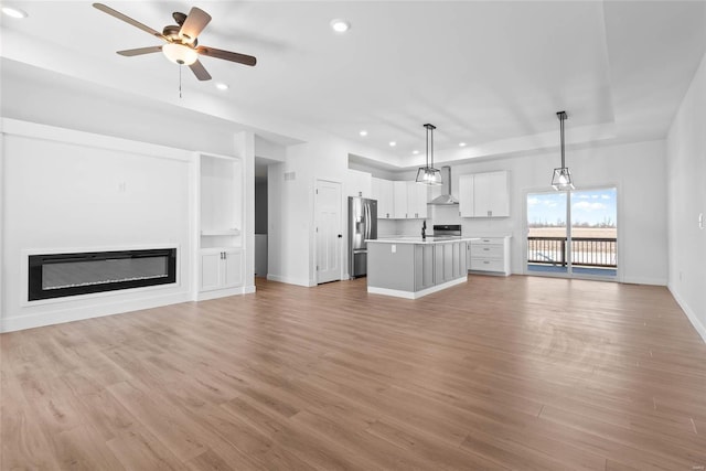 unfurnished living room with baseboards, a glass covered fireplace, light wood-style flooring, ceiling fan, and recessed lighting