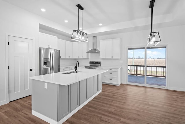 kitchen featuring stainless steel appliances, a sink, white cabinetry, light countertops, and wall chimney exhaust hood