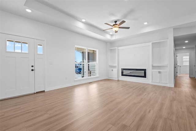 unfurnished living room with light wood-type flooring, a raised ceiling, a wealth of natural light, and a glass covered fireplace