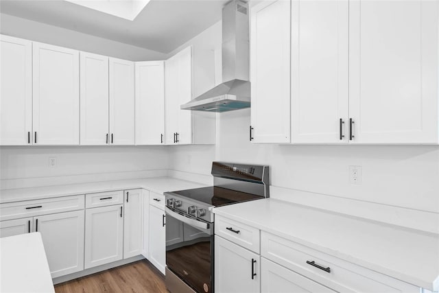 kitchen with stainless steel electric range oven, wall chimney exhaust hood, white cabinetry, and light countertops