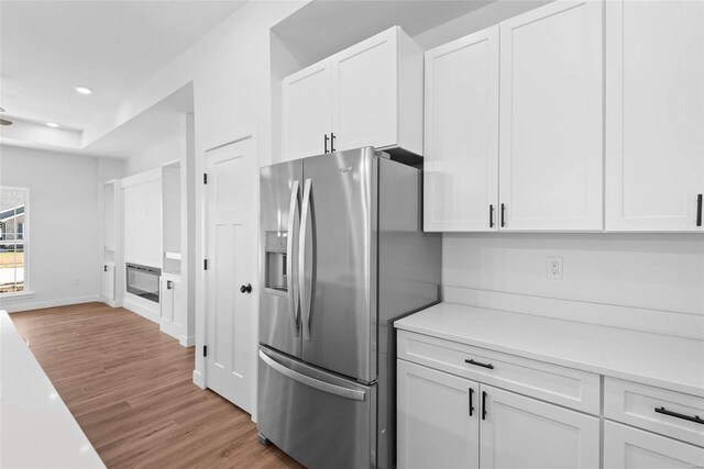 kitchen with light countertops, white cabinets, light wood finished floors, and stainless steel fridge with ice dispenser