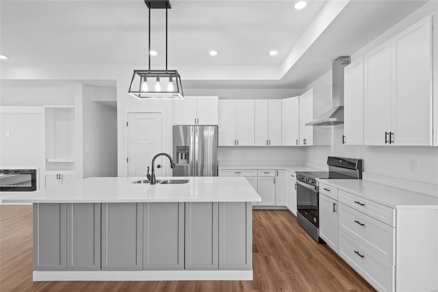 kitchen featuring stainless steel appliances, light countertops, a center island with sink, and wall chimney exhaust hood