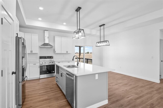 kitchen featuring light wood-style flooring, stainless steel appliances, a sink, light countertops, and wall chimney exhaust hood