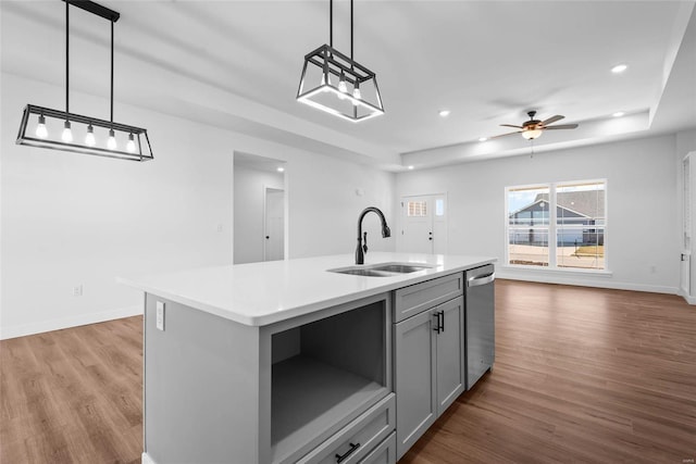 kitchen featuring open floor plan, wood finished floors, a sink, gray cabinetry, and stainless steel dishwasher