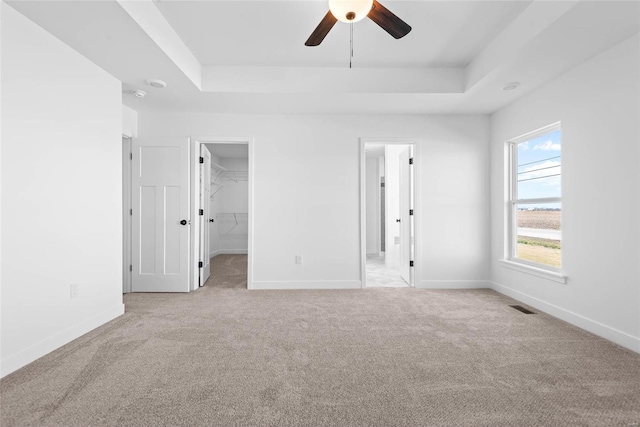 unfurnished bedroom with a raised ceiling, visible vents, a spacious closet, carpet flooring, and baseboards