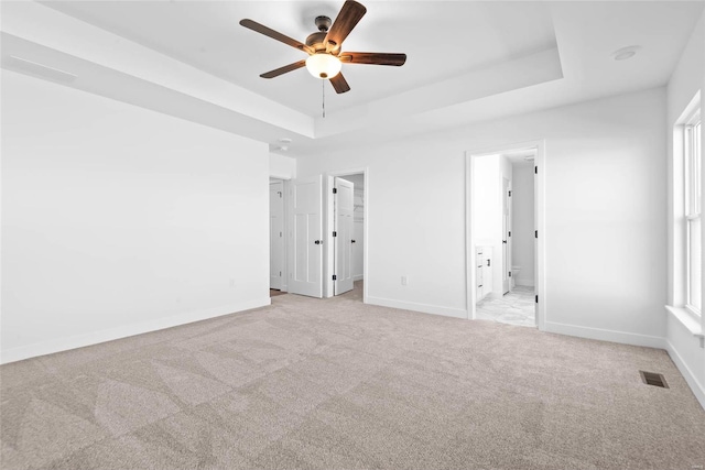 unfurnished bedroom with a raised ceiling, visible vents, light carpet, and baseboards