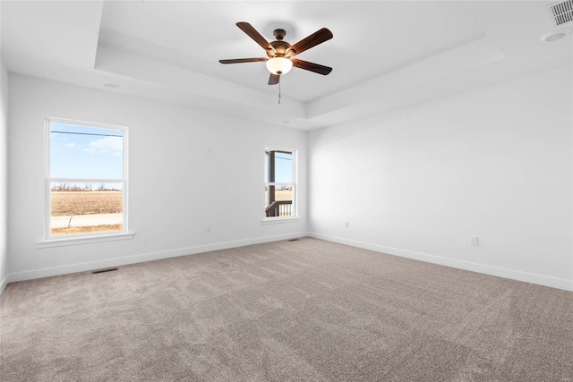 carpeted spare room with a ceiling fan, a tray ceiling, visible vents, and baseboards