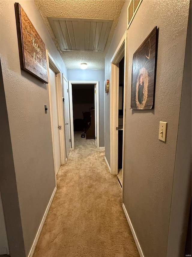 hallway with a textured ceiling, a textured wall, visible vents, and light colored carpet