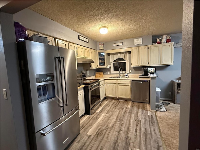 kitchen featuring appliances with stainless steel finishes, light countertops, a textured ceiling, under cabinet range hood, and a sink