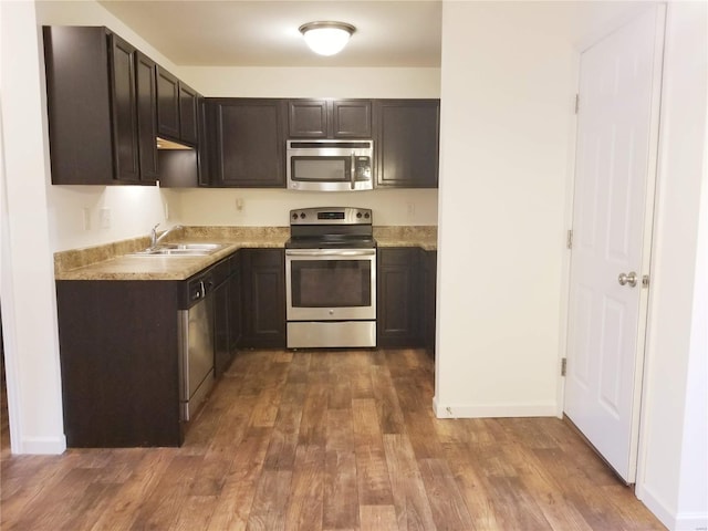 kitchen with dark wood-style floors, stainless steel appliances, light countertops, a sink, and dark brown cabinets