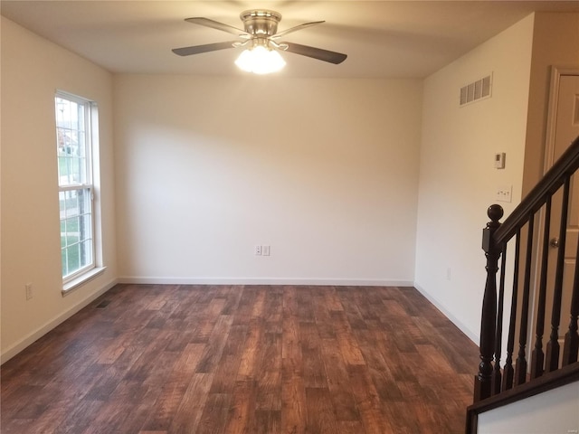 empty room with dark wood-type flooring, visible vents, stairway, and baseboards