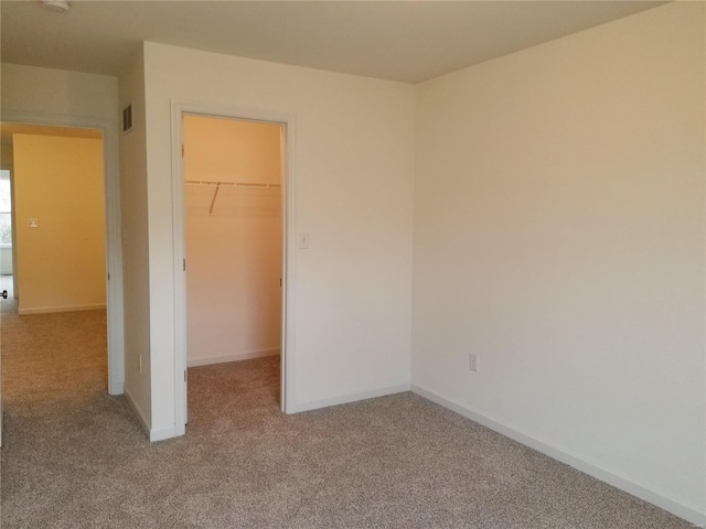 unfurnished bedroom featuring carpet floors, a spacious closet, visible vents, and baseboards