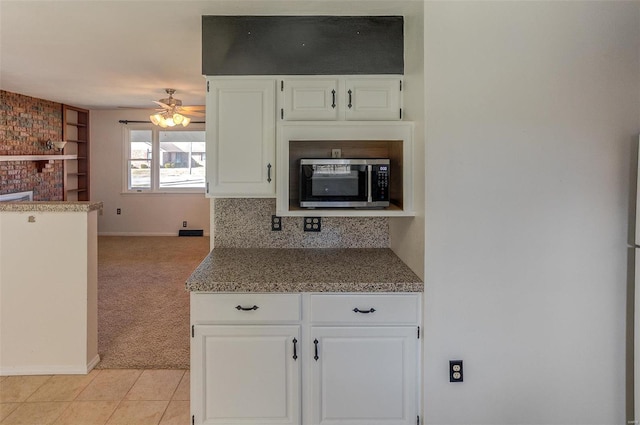 kitchen featuring light carpet, ceiling fan, stainless steel microwave, a fireplace, and white cabinetry