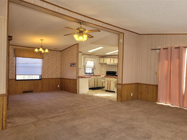 unfurnished living room with a textured ceiling, light carpet, ornamental molding, wainscoting, and wallpapered walls