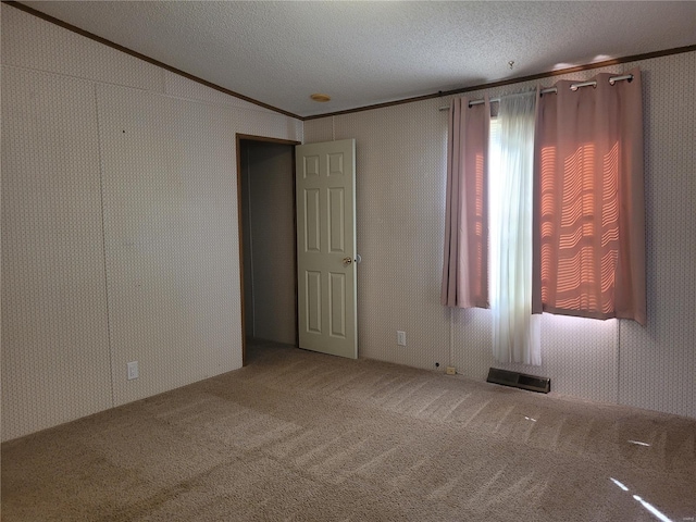 empty room with carpet floors, a textured ceiling, visible vents, and crown molding