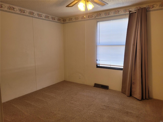 carpeted empty room with a ceiling fan, a healthy amount of sunlight, visible vents, and a textured ceiling