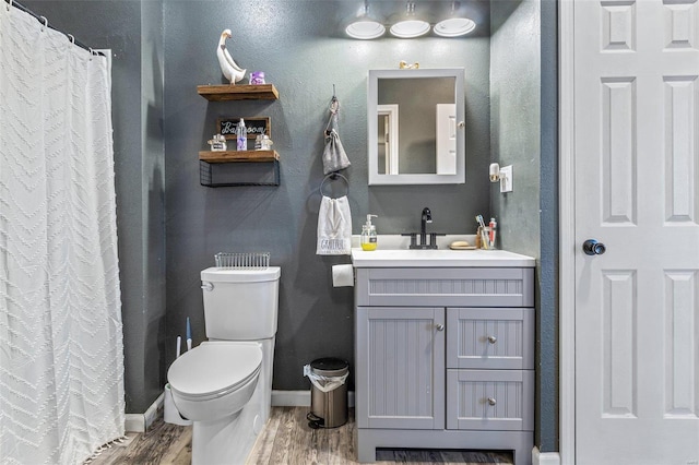 bathroom with toilet, vanity, baseboards, and wood finished floors