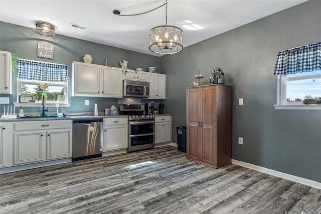 kitchen with visible vents, baseboards, appliances with stainless steel finishes, wood finished floors, and a sink