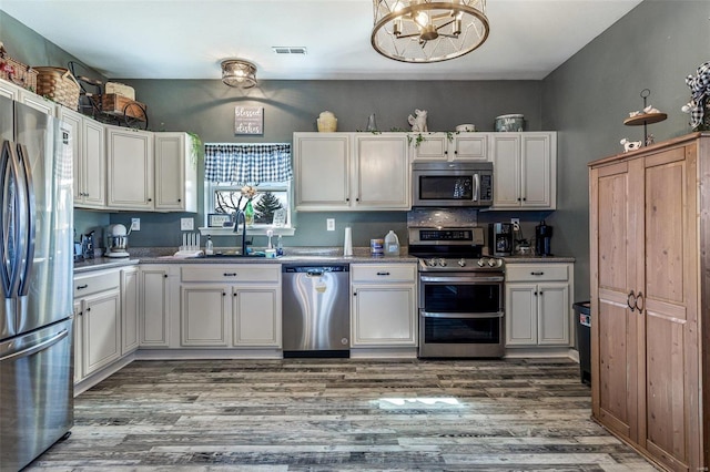 kitchen featuring visible vents, wood finished floors, a notable chandelier, stainless steel appliances, and a sink