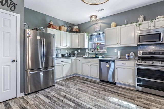 kitchen with visible vents, light wood-style flooring, white cabinets, stainless steel appliances, and a sink