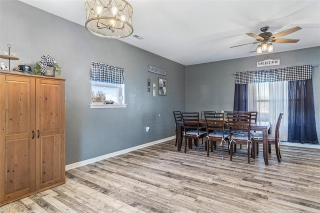 dining space featuring light wood-style flooring, plenty of natural light, ceiling fan with notable chandelier, and baseboards