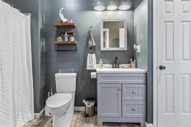 bathroom with vanity, wood finished floors, baseboards, toilet, and a textured wall