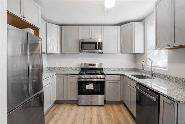 kitchen featuring light stone counters, gray cabinetry, a sink, appliances with stainless steel finishes, and light wood-type flooring