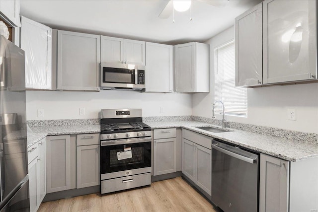 kitchen with gray cabinetry, appliances with stainless steel finishes, a sink, and light wood-style floors