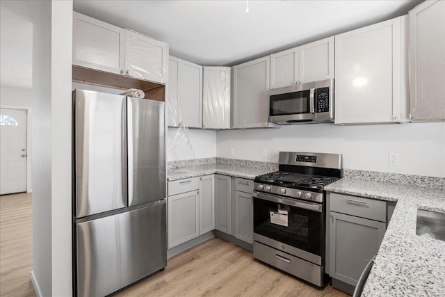 kitchen with light stone countertops, light wood finished floors, appliances with stainless steel finishes, and gray cabinets