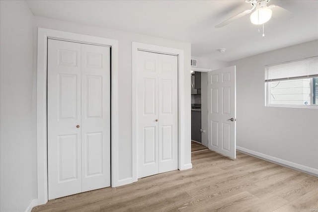 unfurnished bedroom featuring light wood finished floors, visible vents, baseboards, ceiling fan, and two closets