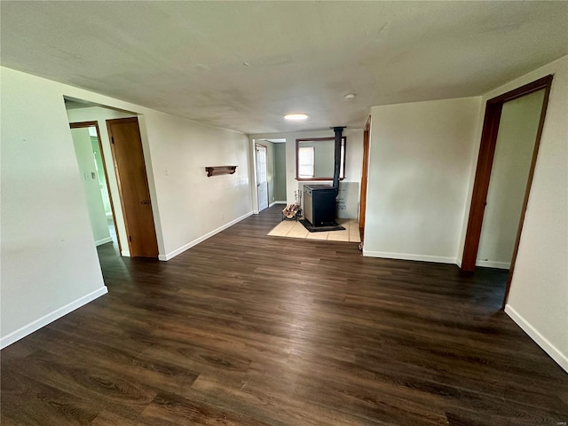 empty room featuring wood finished floors, a wood stove, and baseboards