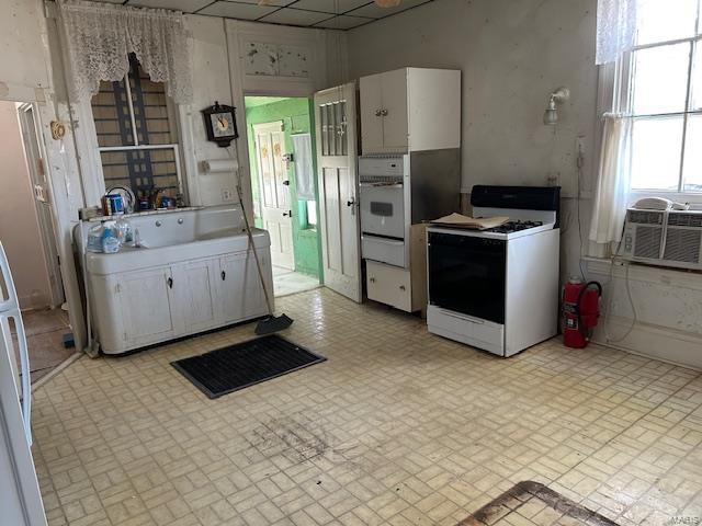 kitchen with cooling unit, white appliances, white cabinetry, and brick patterned floor