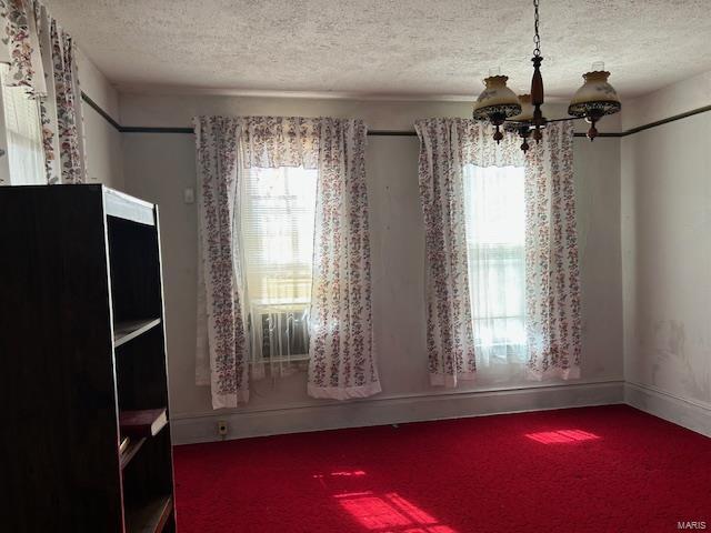 carpeted empty room with a textured ceiling, baseboards, and a notable chandelier