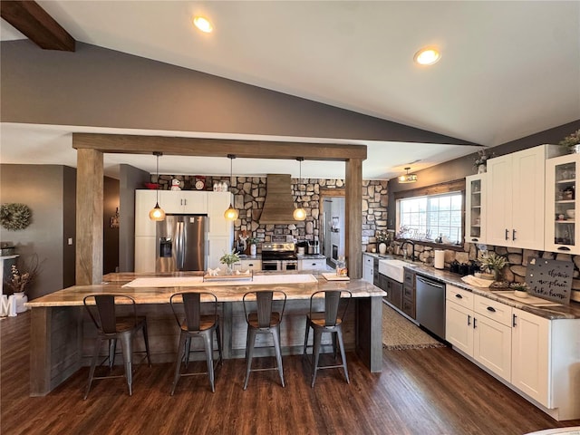 kitchen with vaulted ceiling with beams, a sink, a kitchen breakfast bar, appliances with stainless steel finishes, and glass insert cabinets