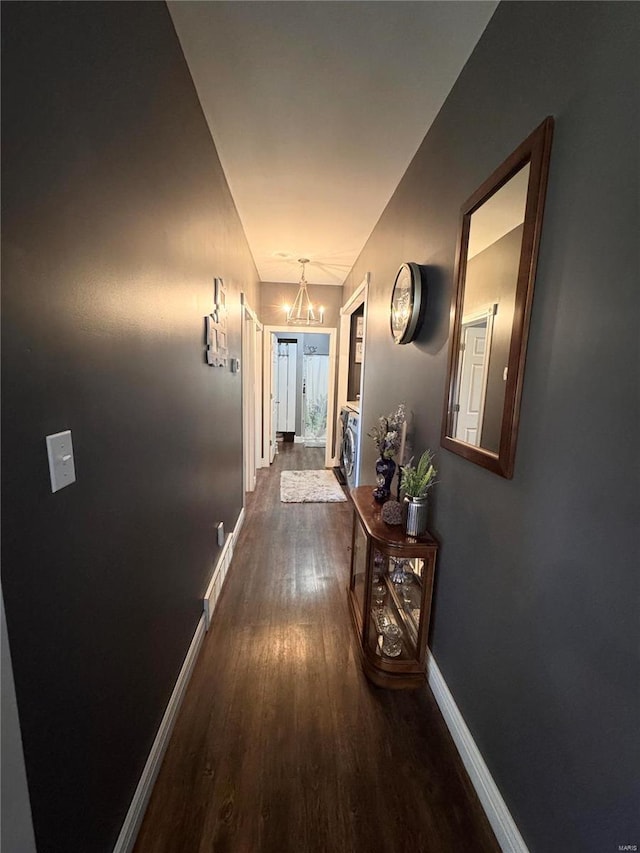 hall featuring baseboards, a chandelier, and dark wood-type flooring