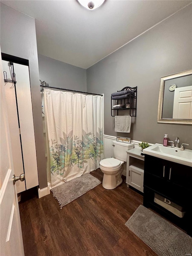 full bath with toilet, a wainscoted wall, a shower with shower curtain, wood finished floors, and vanity