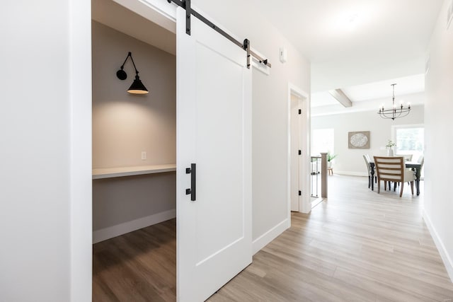 hallway with baseboards, a notable chandelier, light wood finished floors, and a barn door