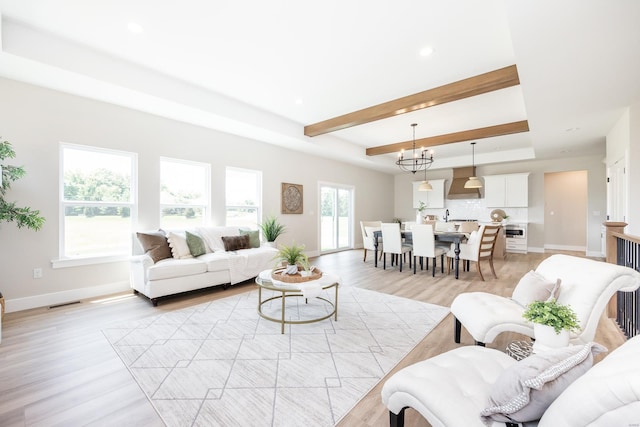 living area with light wood finished floors, a raised ceiling, and an inviting chandelier