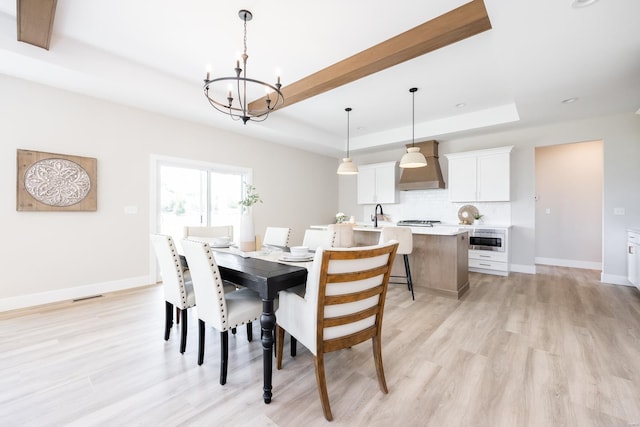 dining space with visible vents, baseboards, light wood finished floors, a raised ceiling, and an inviting chandelier