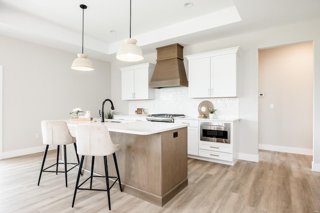 kitchen with a kitchen island with sink, a sink, custom exhaust hood, range, and a raised ceiling