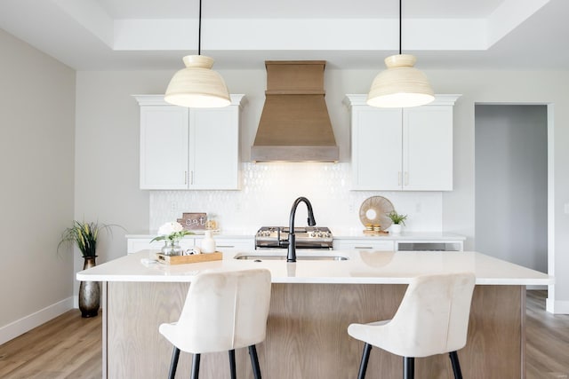 kitchen with light wood-style flooring, premium range hood, a kitchen breakfast bar, backsplash, and a tray ceiling