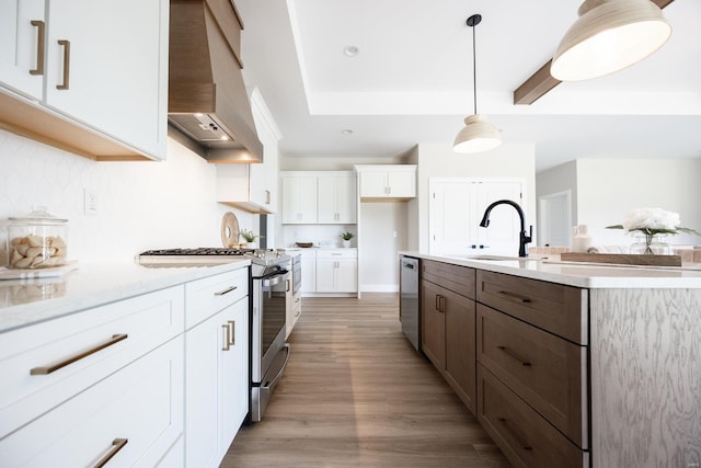 kitchen featuring stainless steel appliances, premium range hood, a sink, white cabinetry, and light wood finished floors